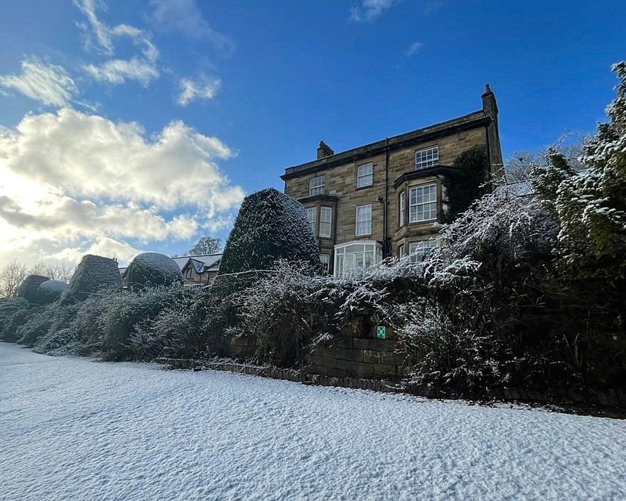 A stone school building and gardens covered in snow under a bright blue winter sky.