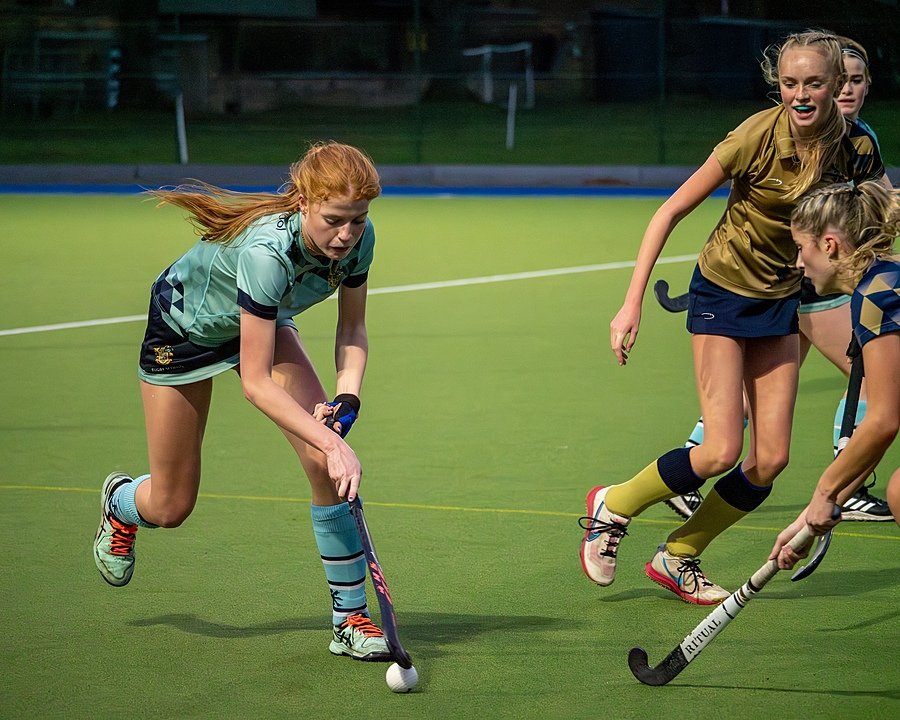 A red-haired girl in a hockey match, attacking two defending girls