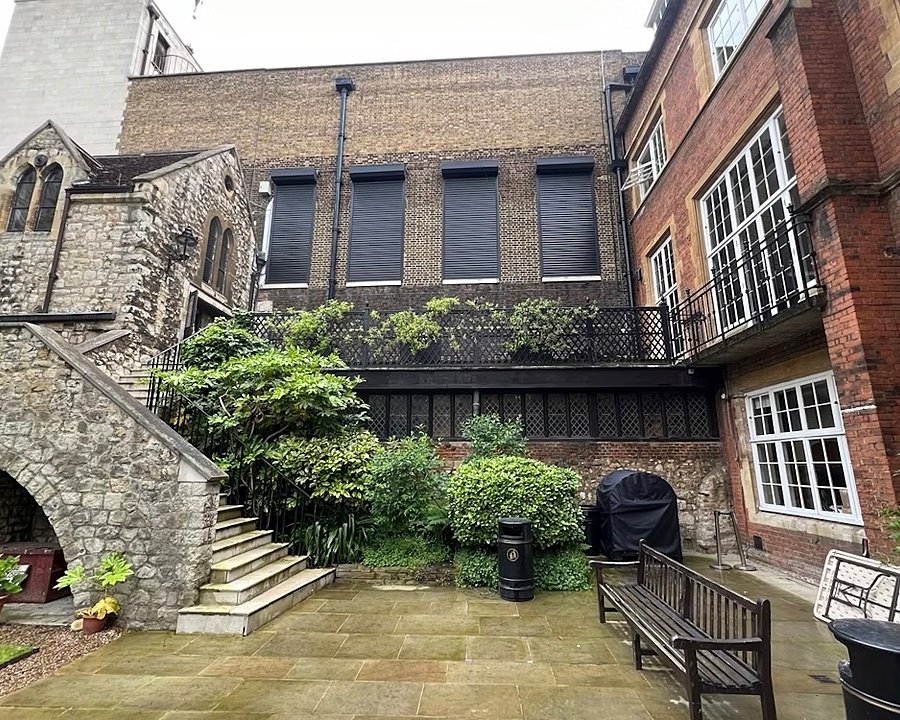 Stone courtyard with stairs leading up to brick and stone buildings covered in greenery.