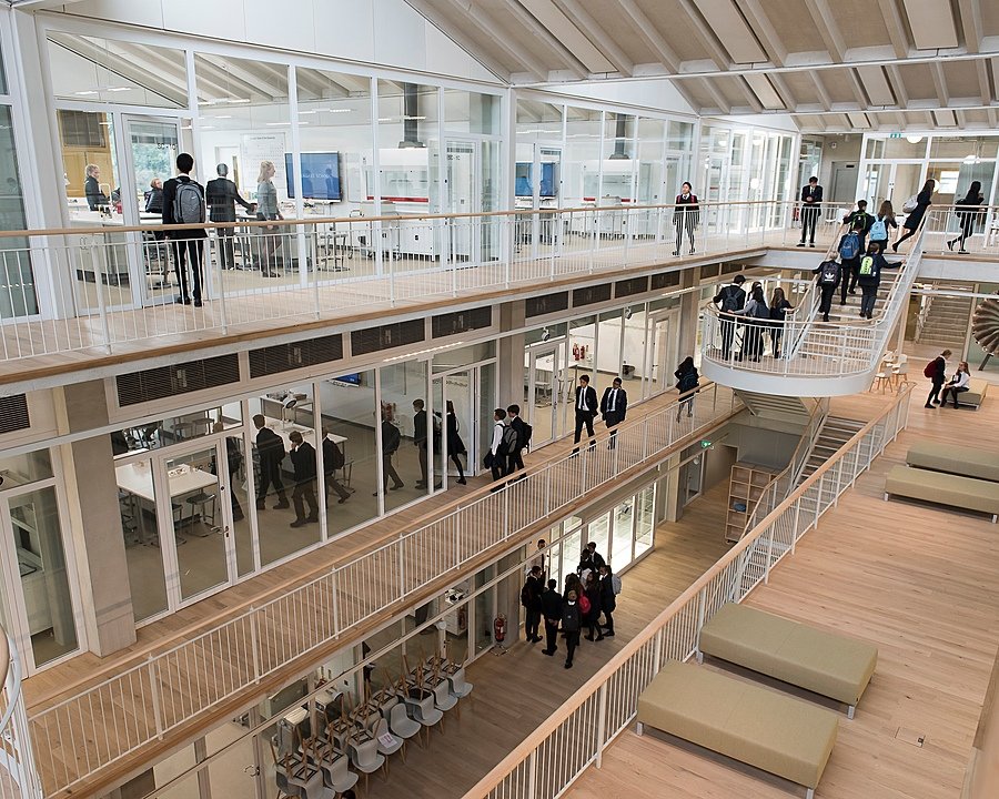 A bright, modern school building with open corridors, glass classrooms, and students walking between floors.