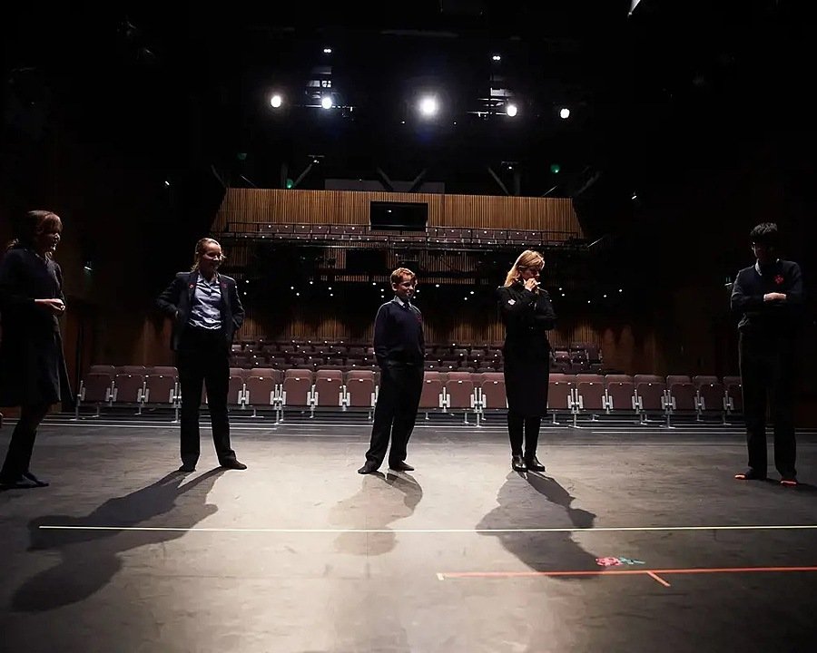 Five pupils on a darkened theatre stage in the process of practicing a theatre play