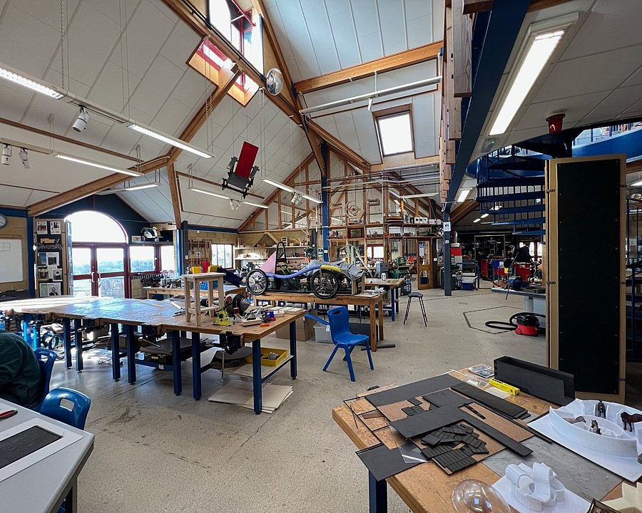 Spacious workshop with high ceilings, workbenches, and student engineering projects on display.