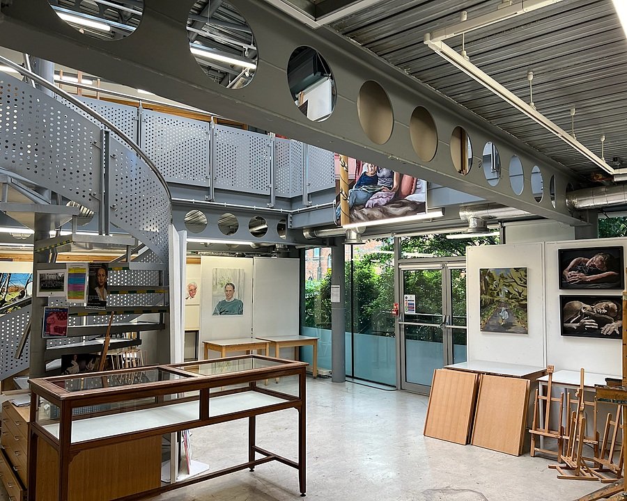Modern art studio with metal beams, a spiral staircase, and paintings displayed on white walls.