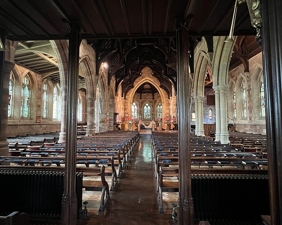Beautiful chapel interior with arched stone columns, stained-glass windows, and rows of wooden pews leading to an ornate altar.
