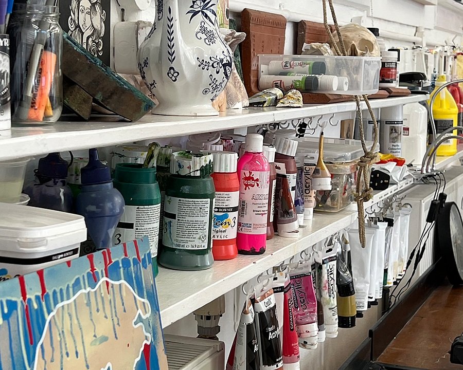 Shelves filled with paint in bottles, glue sticks and other art equipment