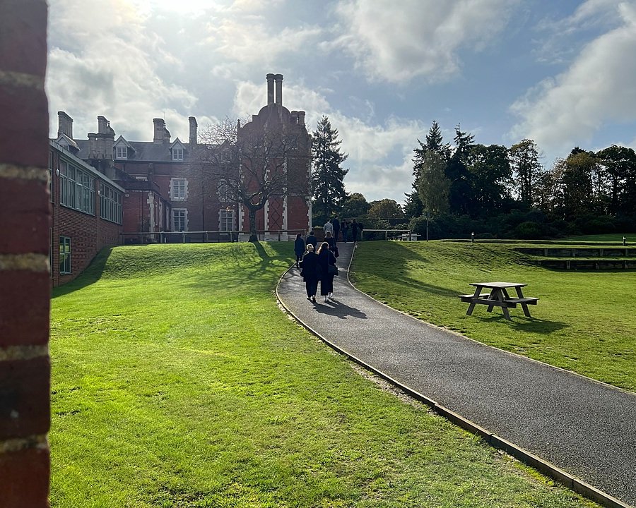A sunny day in which a group of ladies is walking along a path towards a large school building