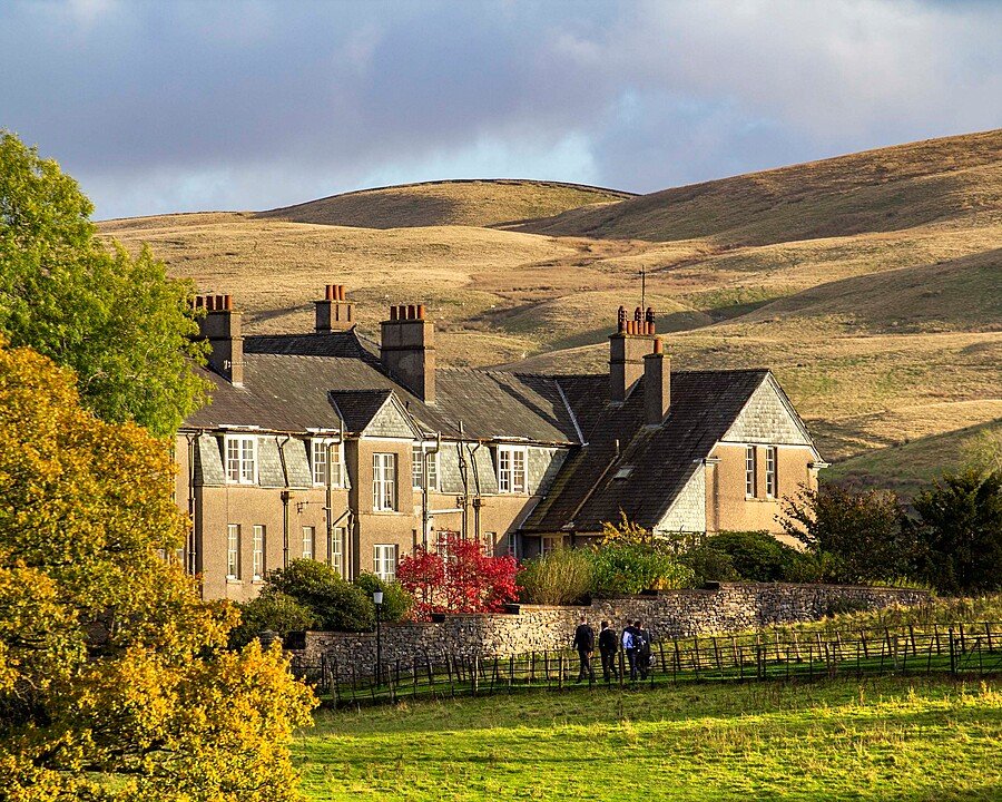 A traditional stone school building surrounded by autumn trees and rolling hills.