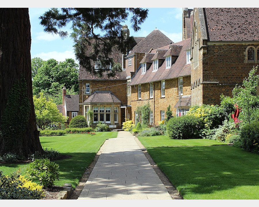 A paved path leading through a landscaped garden to a historic brick building with gabled roofs.