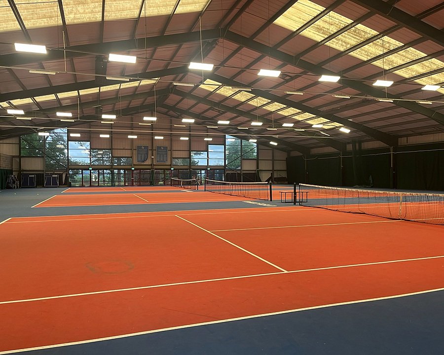Spacious indoor tennis courts with bright lighting and red-and-blue flooring.