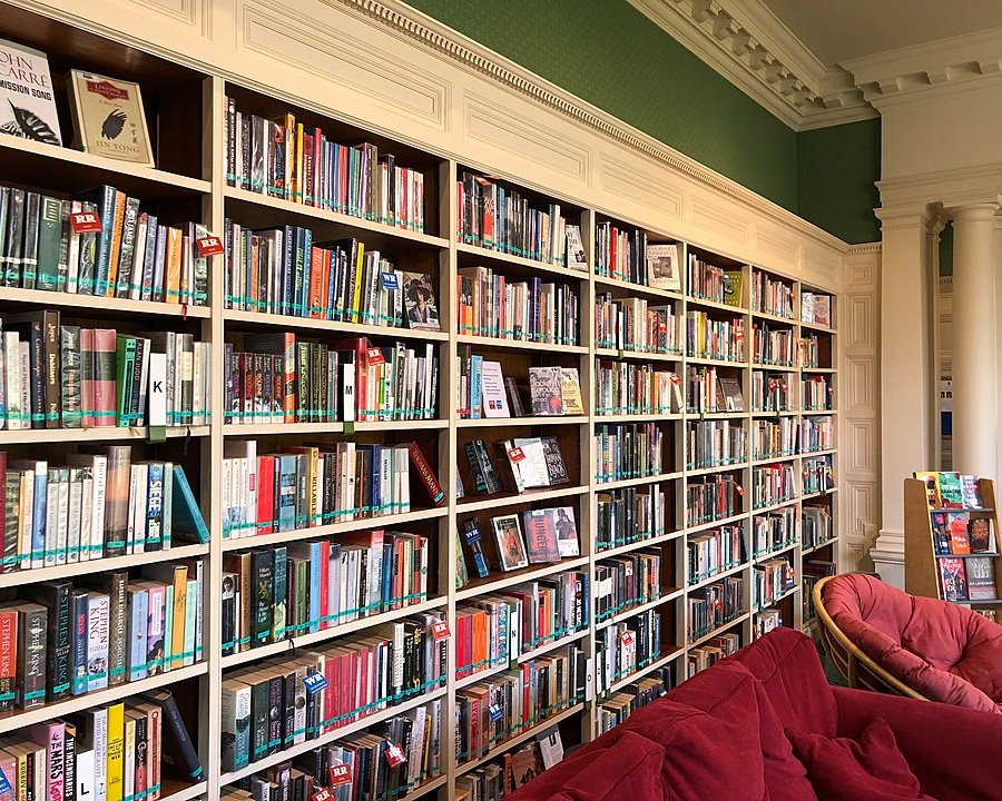 Massive book shelf with books and a cozy red sofa in front