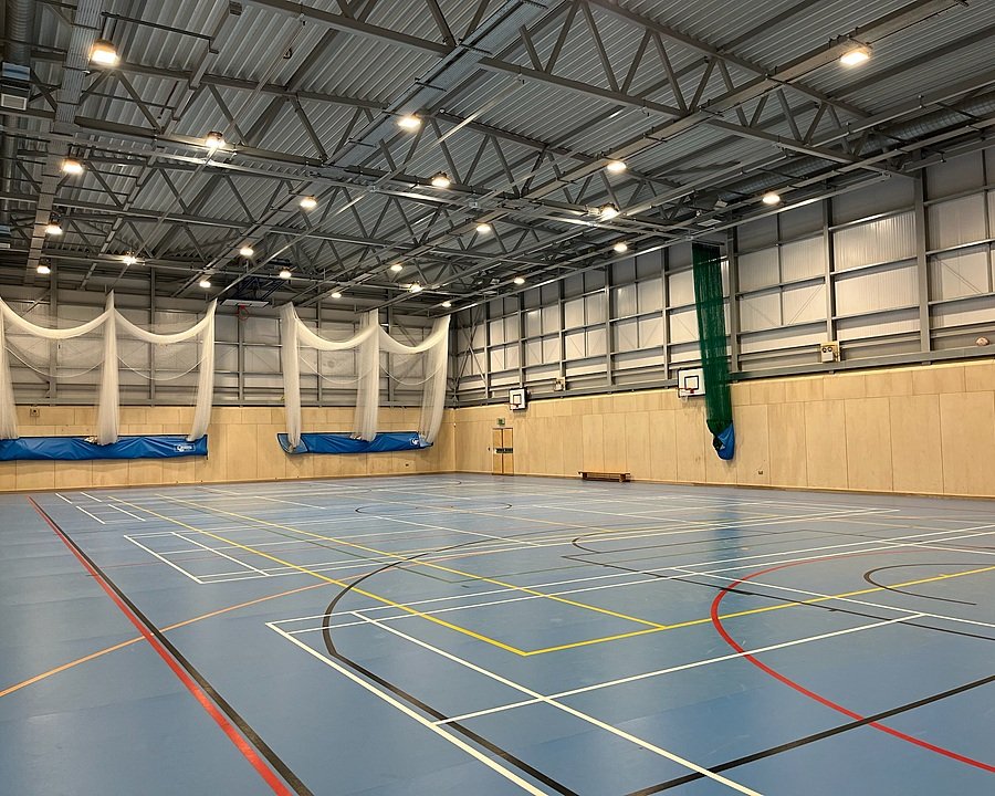 A well-lit, modern sports hall with basketball hoops and cricket nets