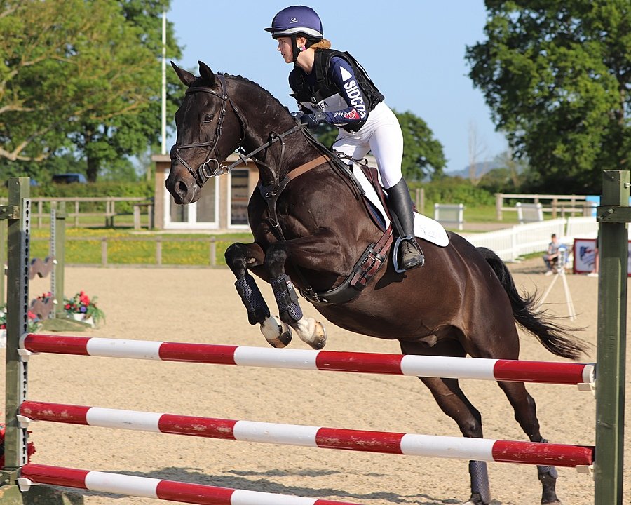 pupil on horseback clearing a red and white jump during an equestrian event.
