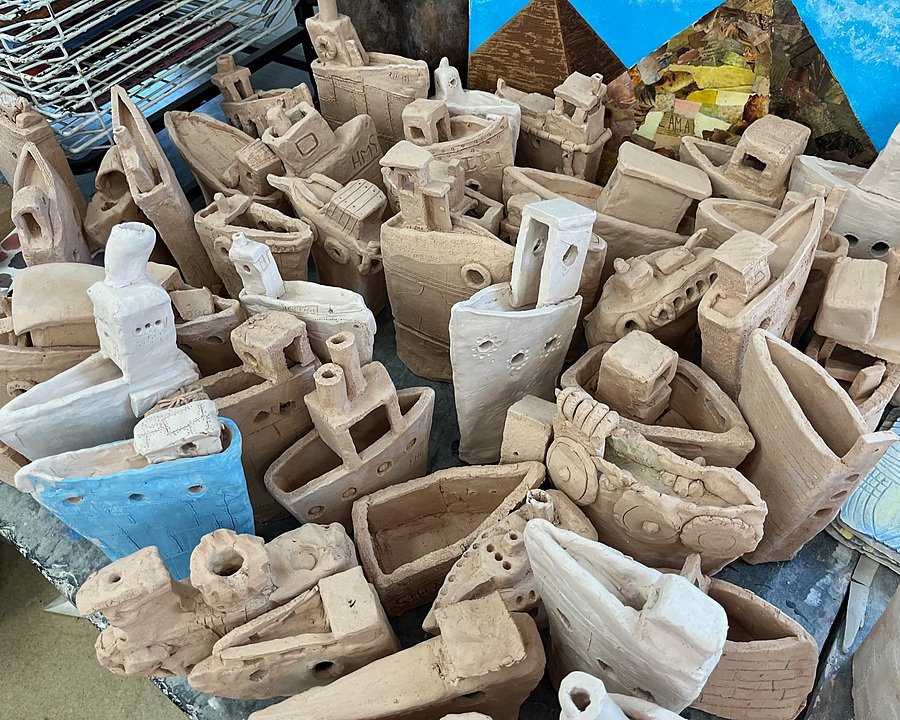Collection of handmade clay boat sculptures displayed together on a table in an art studio.