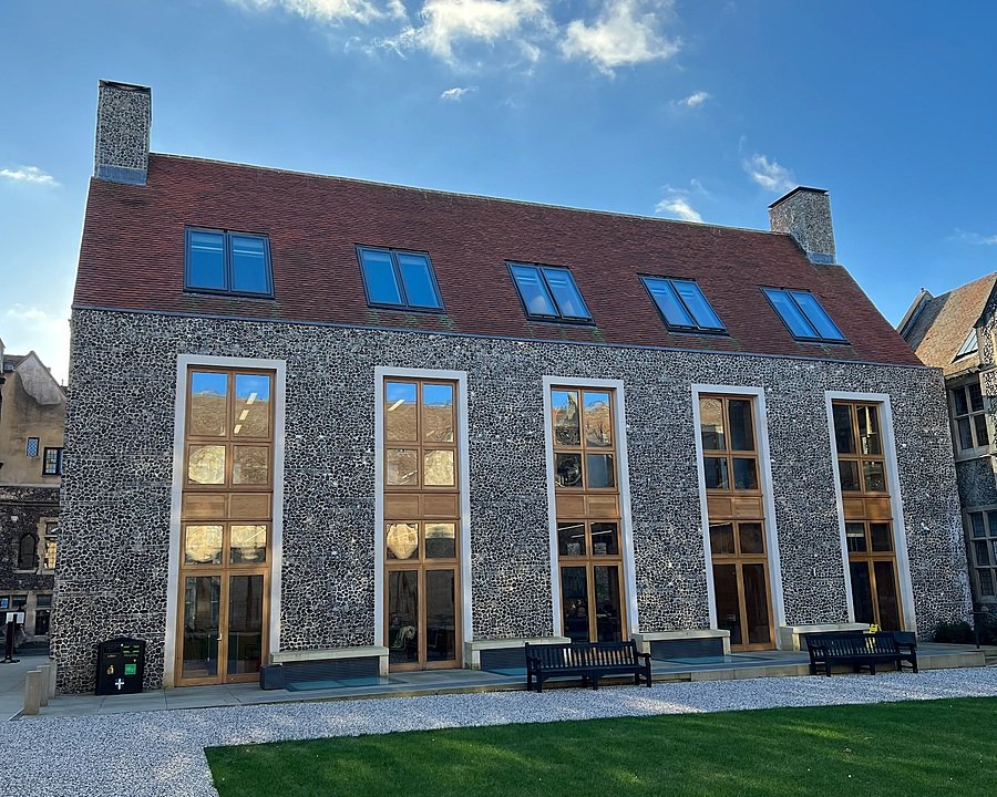 Modern school building with tall stone walls, large wooden-framed windows, and a red-tiled roof.