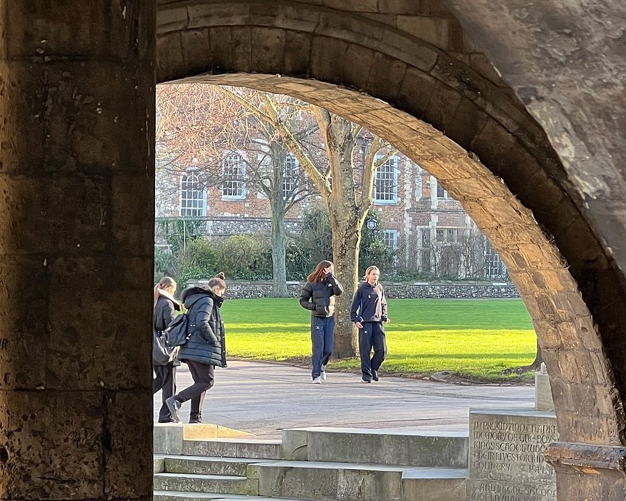 Students walking together across a courtyard seen through a stone archway on a bright day.