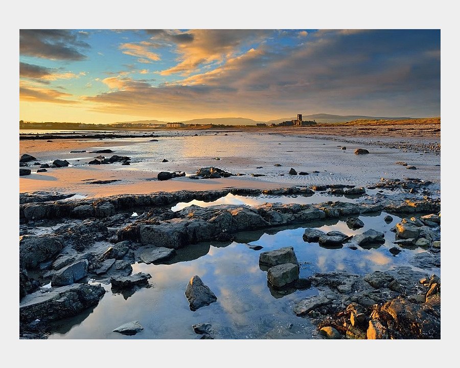 Tide on the beach, lots of rocks and sand and a blue organge sky with clouds