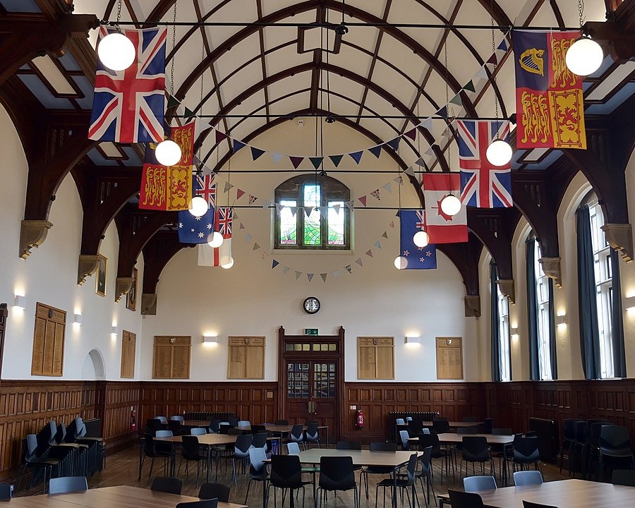 A big dining hall with very high ceiling and wooden beam construction decorated with international flags and buntings