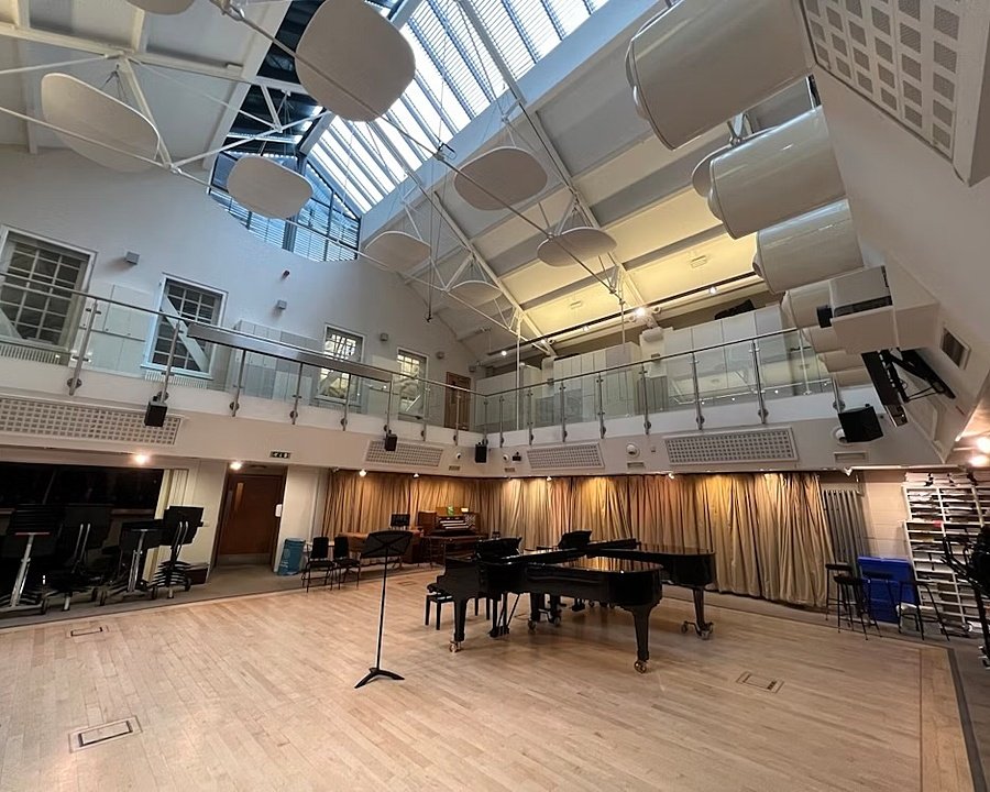 Spacious music hall with grand pianos, high ceiling, and acoustic panels under a glass roof.