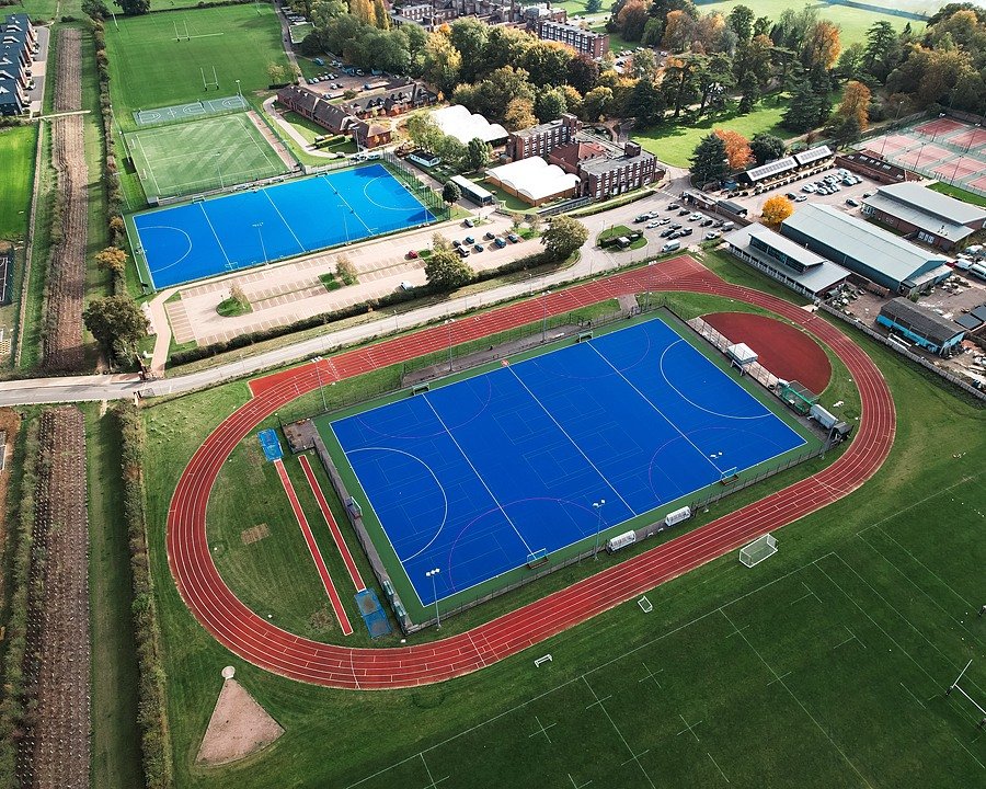 Aerial view of a blue hockey pitch and surrounding sports facilities on the school campus.