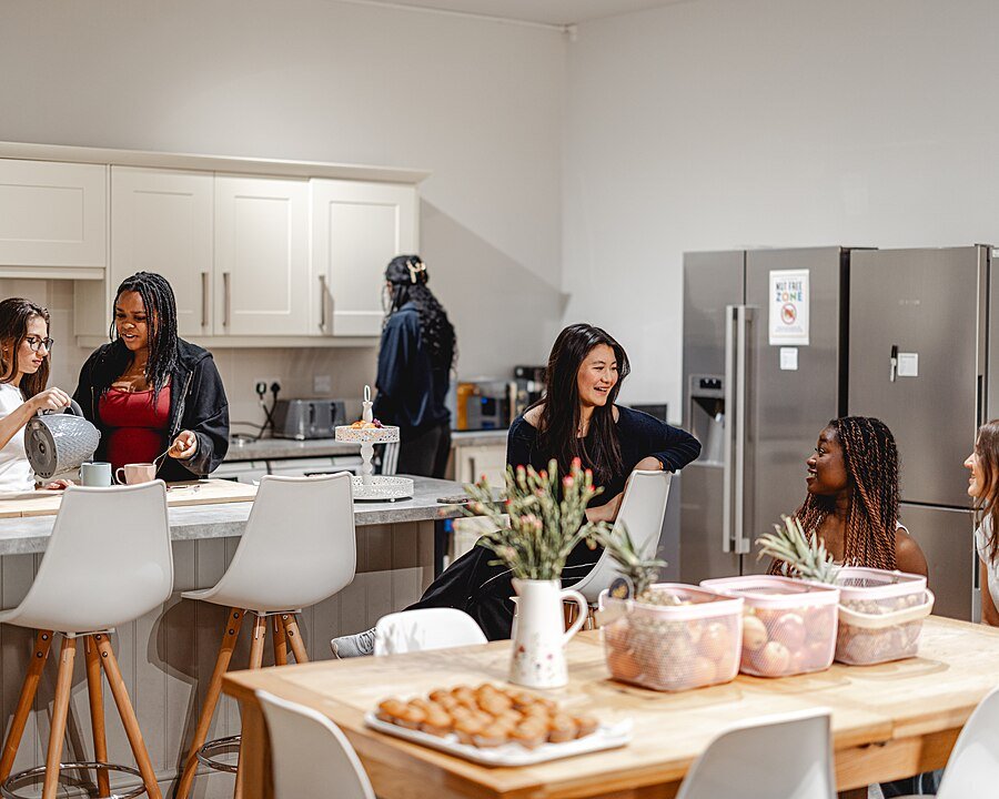 Students sitting together at a table in a modern boarding house kitchen.