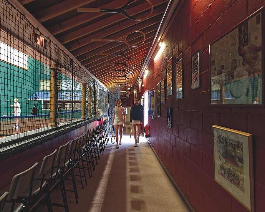 A corridor with real tennis courts on the left and tennis rackets hanging from the ceiling
