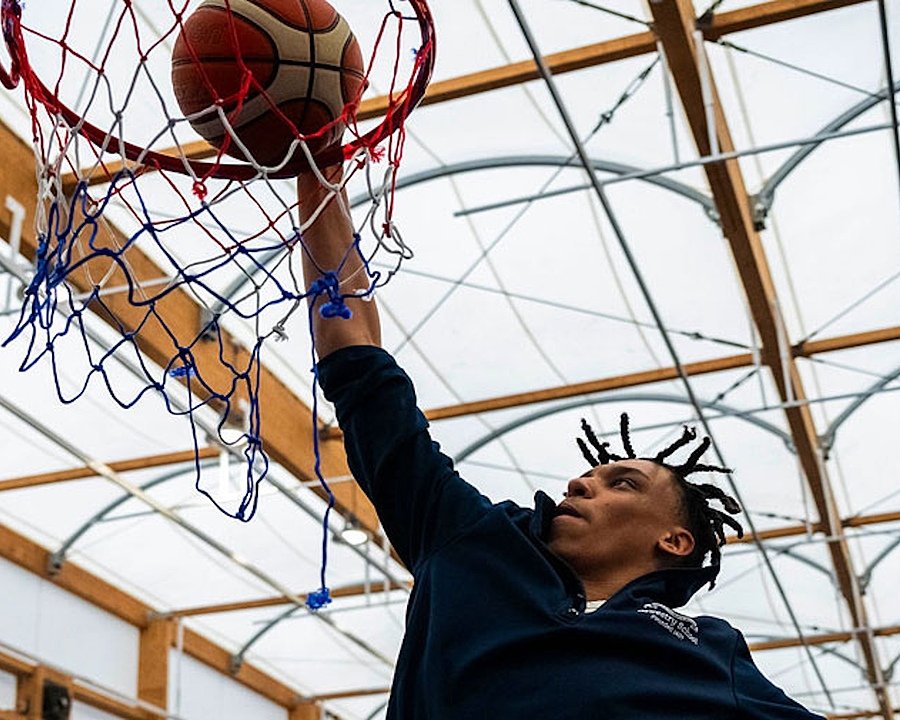 Boy with dreadlocks dunking a basketball into a hoop in a sports hall