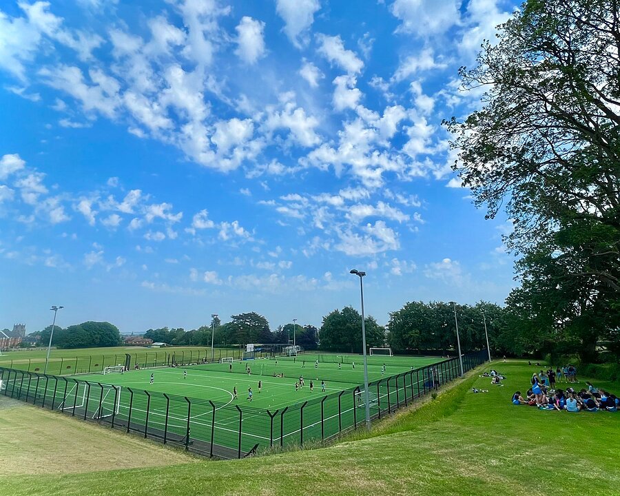 A green astroturf football pitch with pupils playing on a clear-skied day
