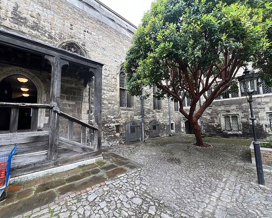 Small stone courtyard with a large tree and old wooden porch entrance.