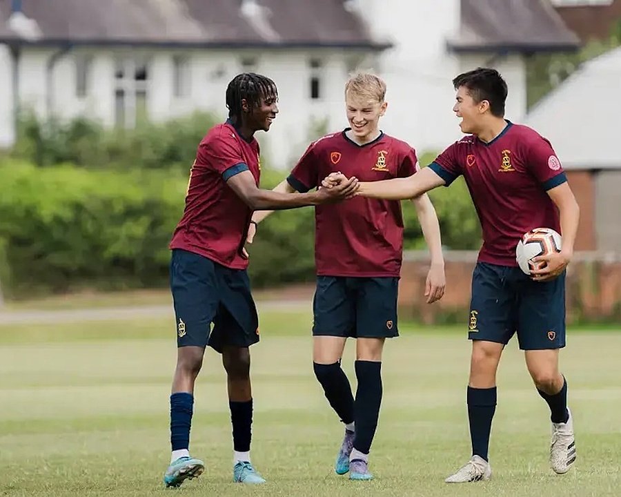 three Football players in their jerseys walking over the pitch laughing, one carrying the football