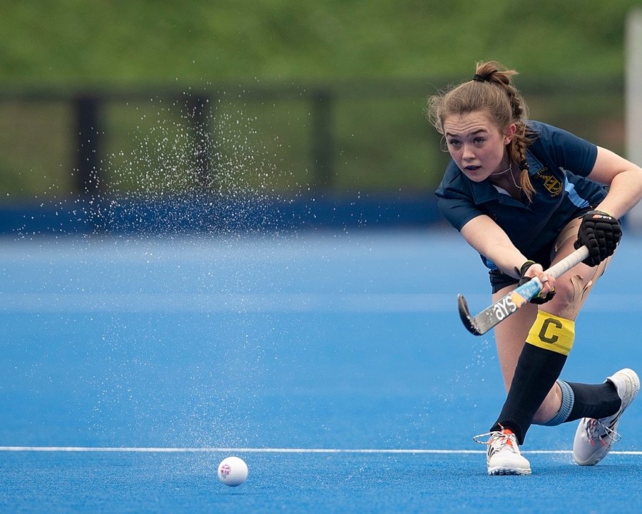 A girl hits the Hockey ball with her stick outside on a blue pitch
