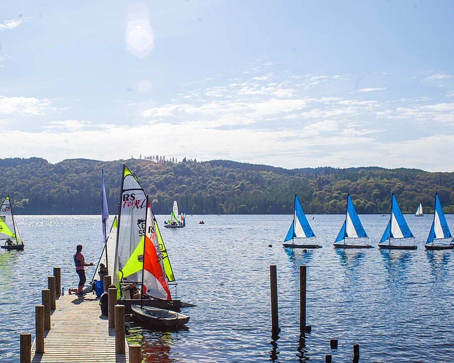 Several students preparing sailing boats on a jetty beside Lake Windermere.
