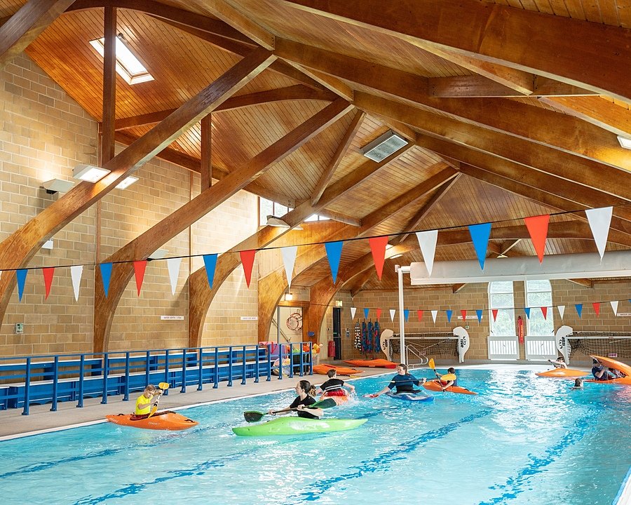 A beautiful indoor swimming pool with wooden beams and students in canoes on the water