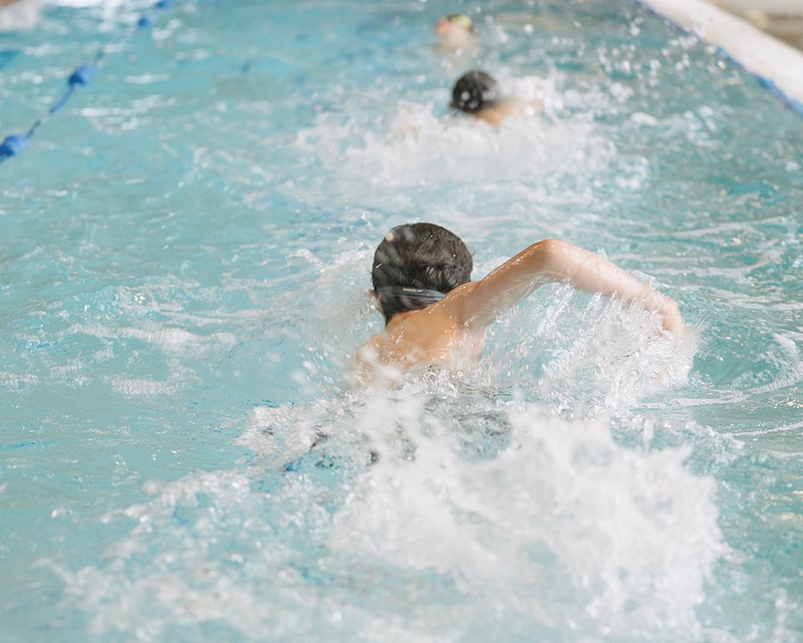 Pupils swimming front crawl during a race in a pool.