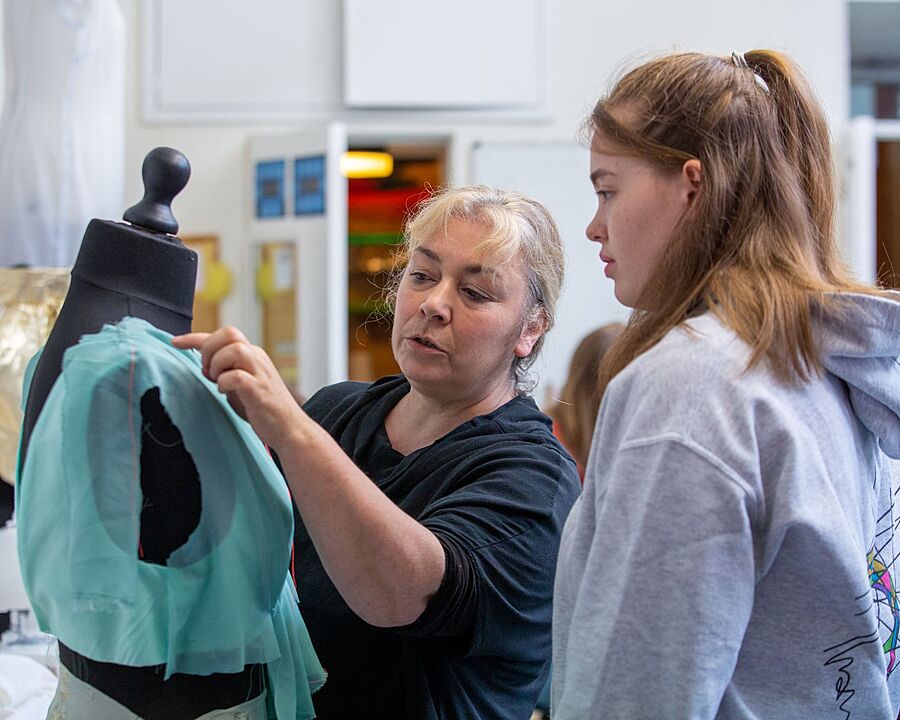 A teacher is showing her student a seam on a piece of fashion on a Judy