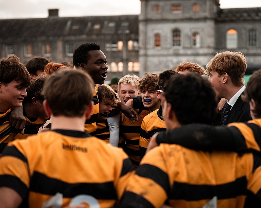 A rugby team in a team huddle cheering together in their orange black team jerseys