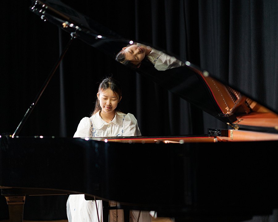 A female student in the spotlight on a dark stage playing the piano