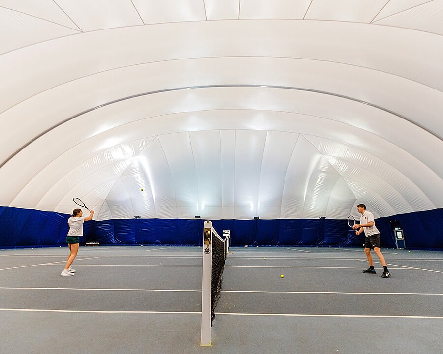 A big indoor tennis court with two players on one of the pitches