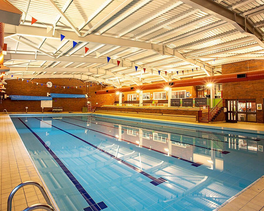 An indoor swimming pool with lanes and spectator seating, lit by bright ceiling lights in a brick-walled facility.