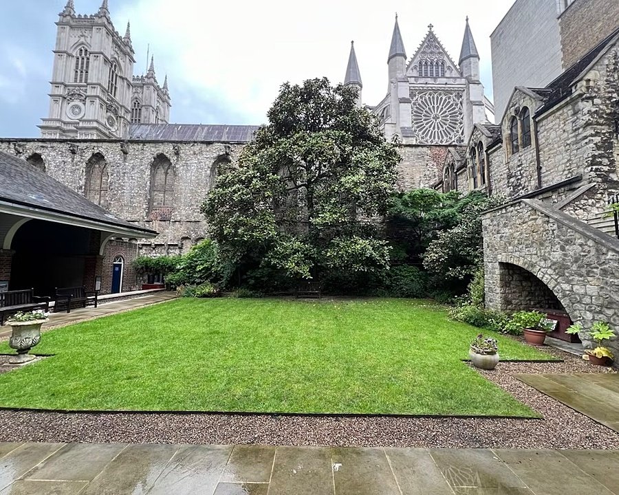 Courtyard garden with neatly cut grass, surrounded by historic stone buildings and cathedral towers in the background.