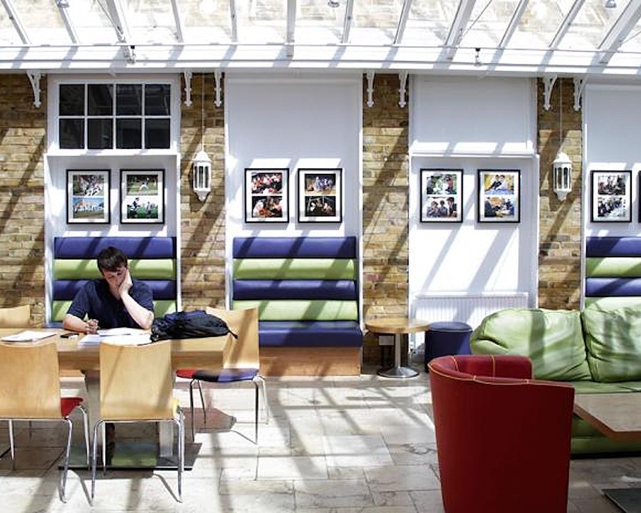 Bright, modern common room with large windows and skylights, brick walls decorated with photos, and colourful seating where a student is studying at a table