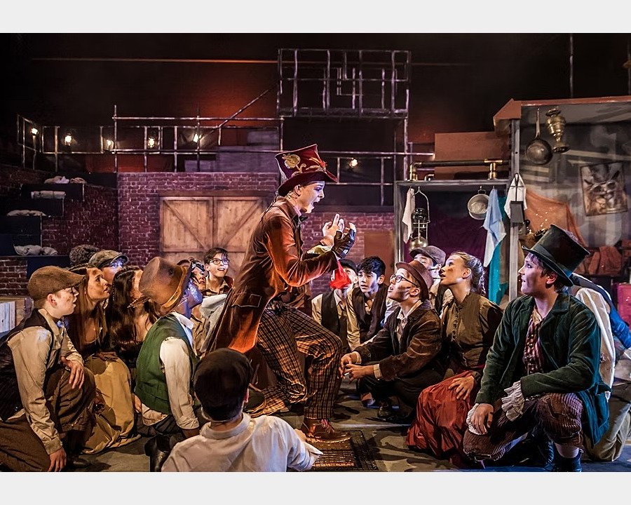 Scene from musical Oliver, boy singing, others in dirty clothes sitting around him