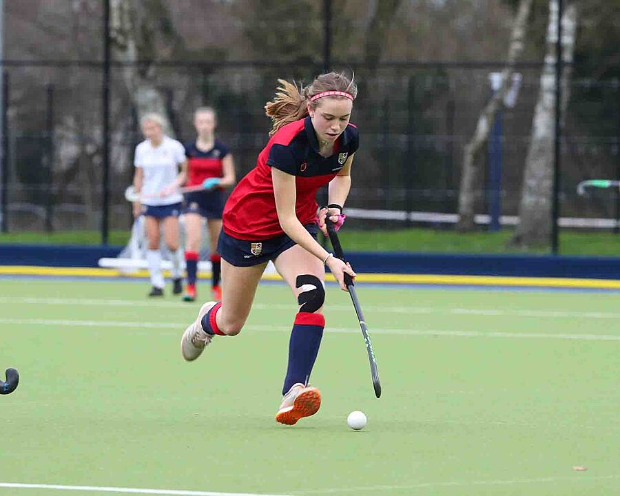A student with her Hockey stick about to hit the ball on the pitch outside