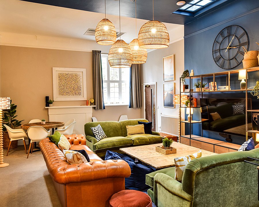 Common room in a boarding house with sofas, armchairs, a coffee table, shelving and ceiling lights.