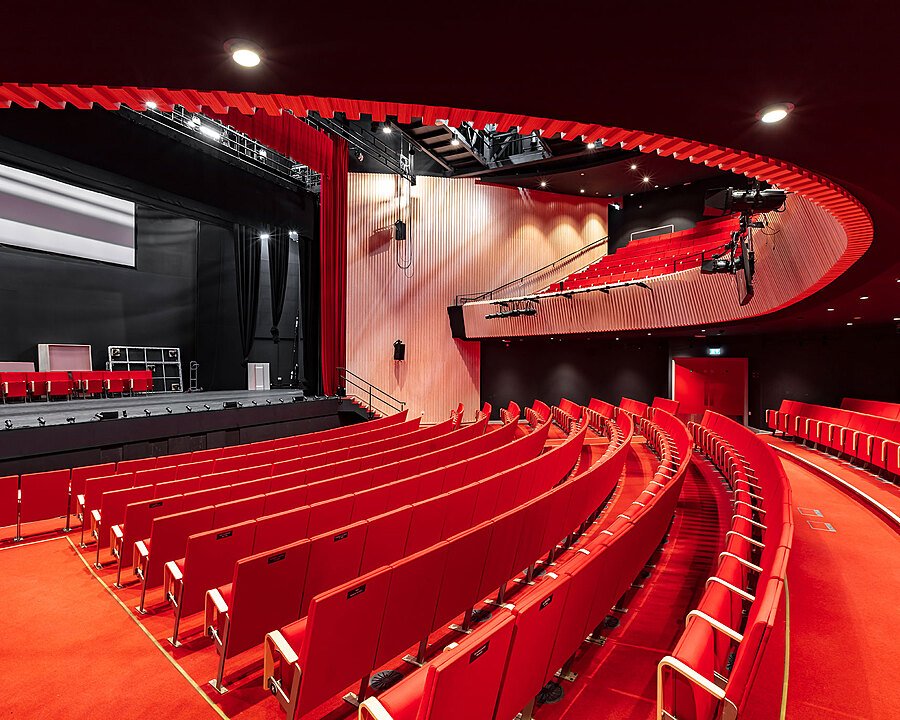 A school Theatre with rows of red chairs in front of a modern stage