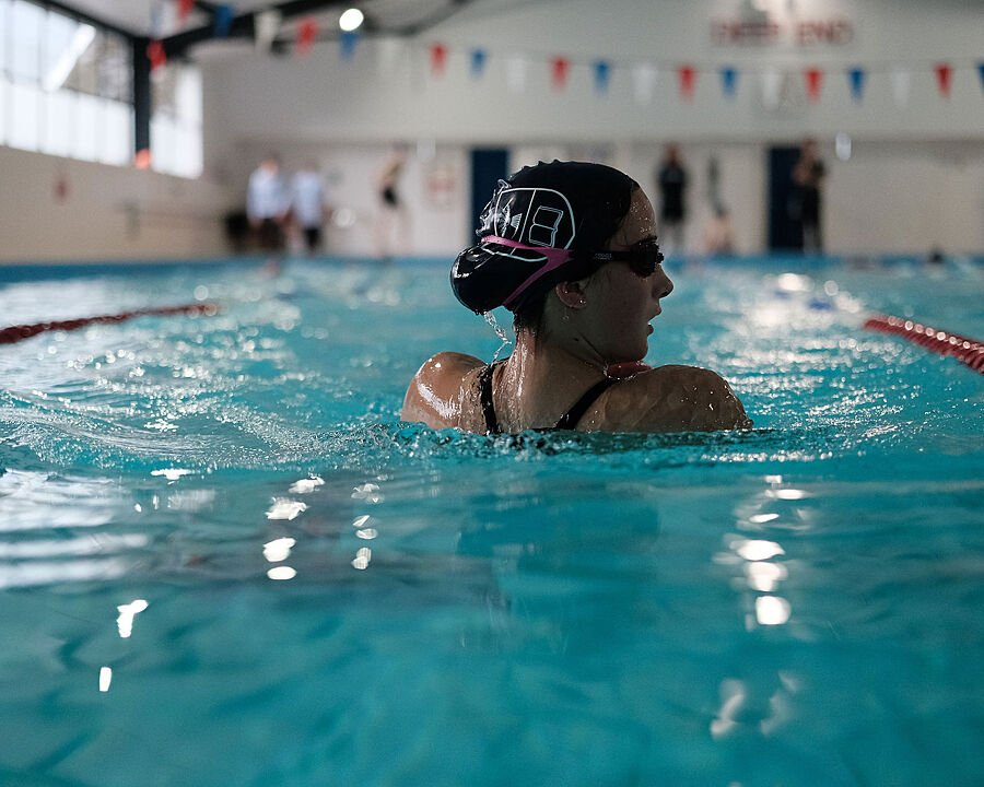 Girl with goggles and swimming cap in a school swimming pool, back to camera