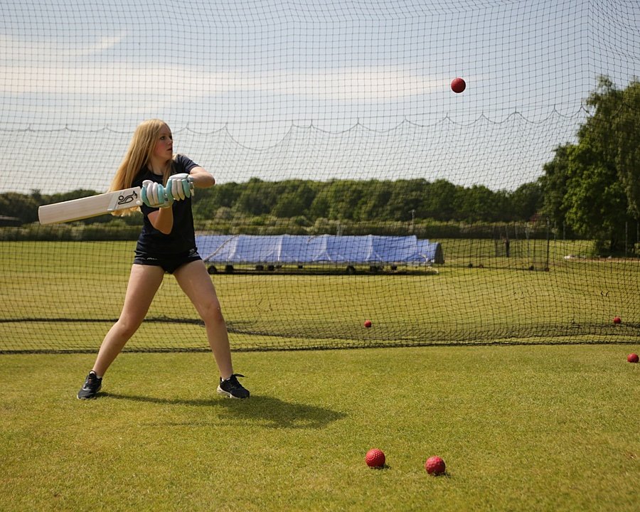 Girl with cricket bat hitting red balls into a net
