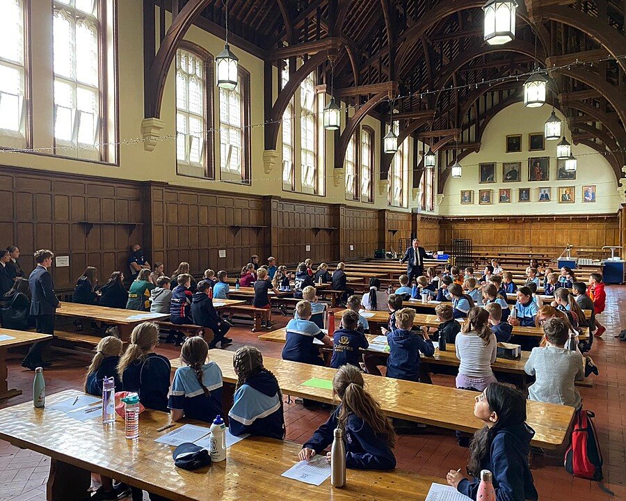 Pupils sitting in a large dining hall with wood beams and at large wood tables