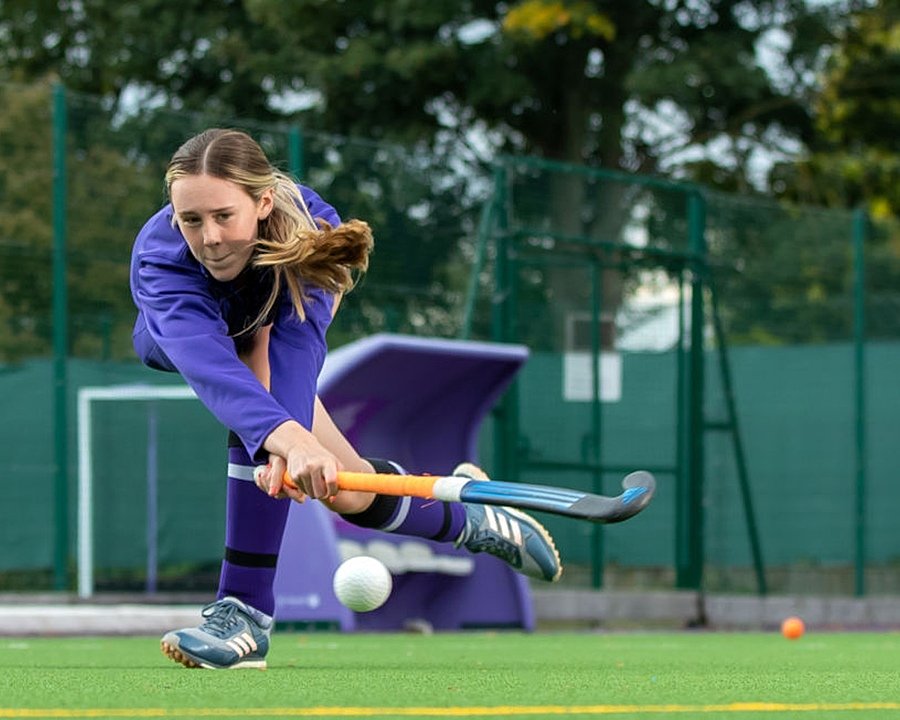 A girl in purple hockey jersey stricking a ball with her stick
