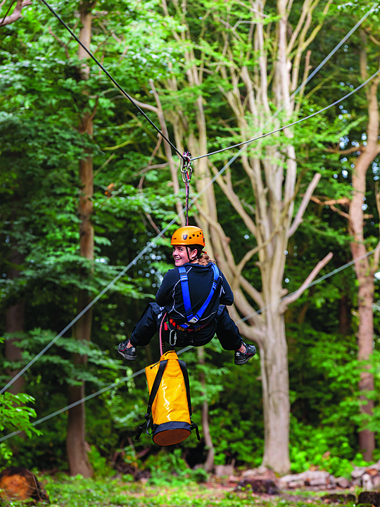 A female student in a climbing harness on a rope in the school's woodland high rope course