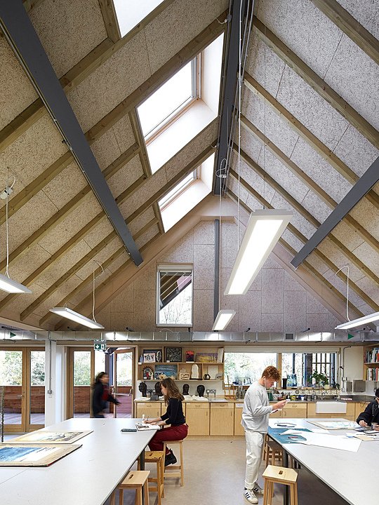 Students working on art and design projects in a well-lit studio with slanted skylights and exposed wooden beams.